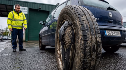 Car tyre with visible inner sidewall bulge and exposed cord threads on wet Irish asphalt outside an NCT test centre